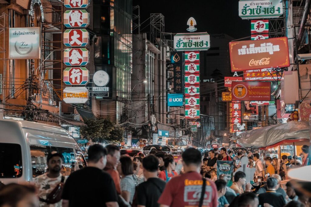 A busy street in Bangkok at night with bright neon signs and a bustling crowd.